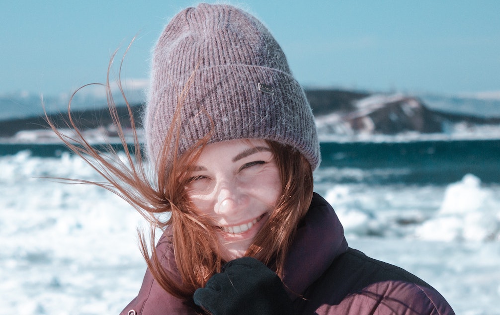 Nainen hymyilee talvimaisemassa harmaa pipo päässä